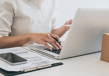Close up of a person holding a pen typing on the computer